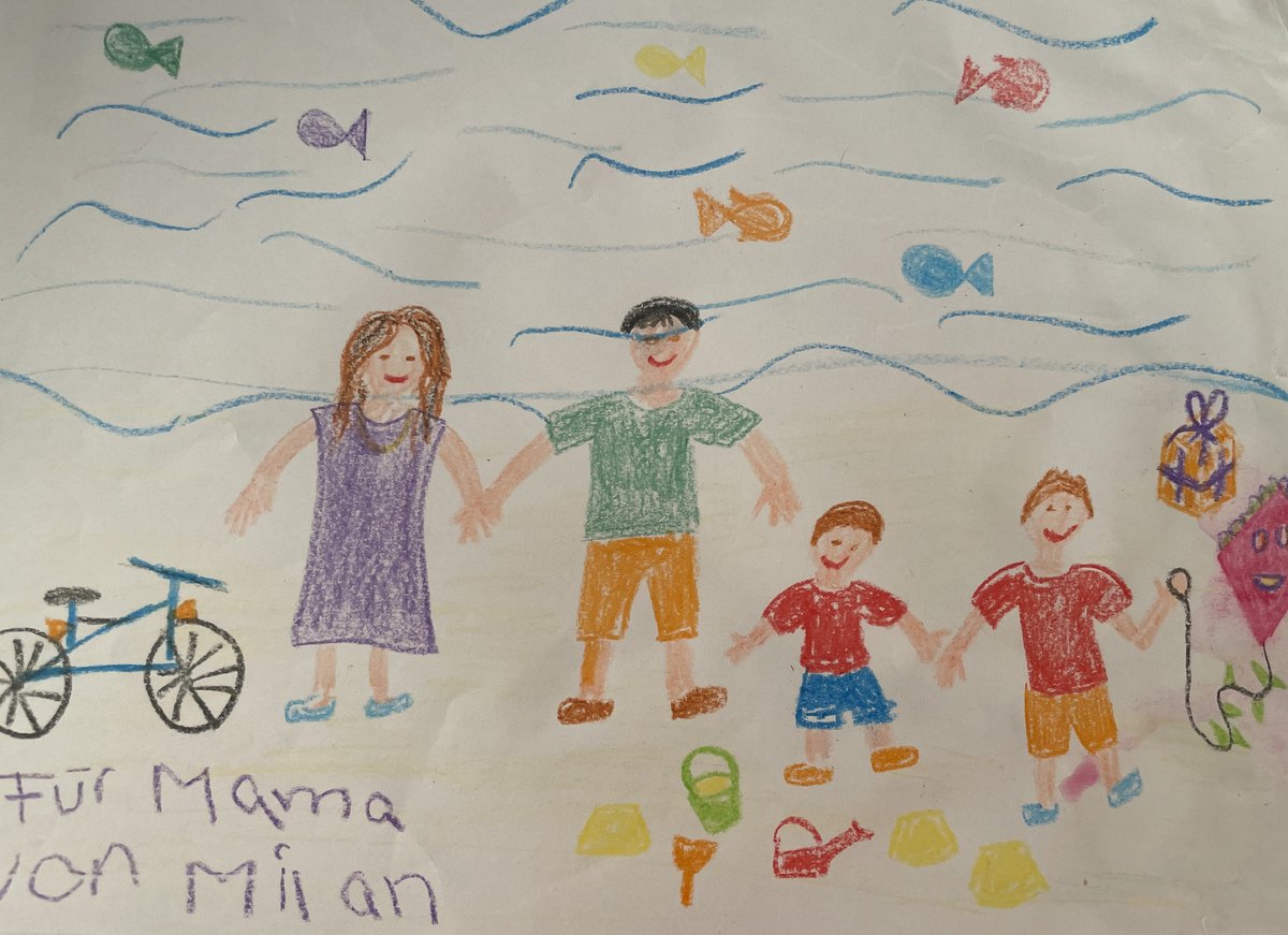 Kinderzeichnung: Familie Hand in Hand am Strand, mit Fischen, Fahrrad und Drachen; in der Ecke steht handschriftlich „Für Mama von Milan“